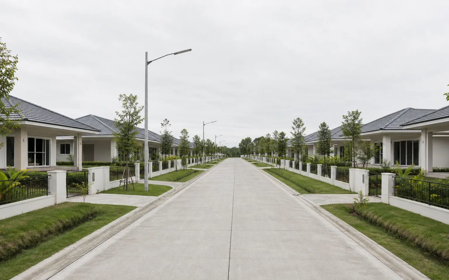 Architectural render: a street inside Ruensuan Lam Luk Ka, single-storey houses set well back on both sides, the road wide, a drainage swale between the footpath and the fence line.